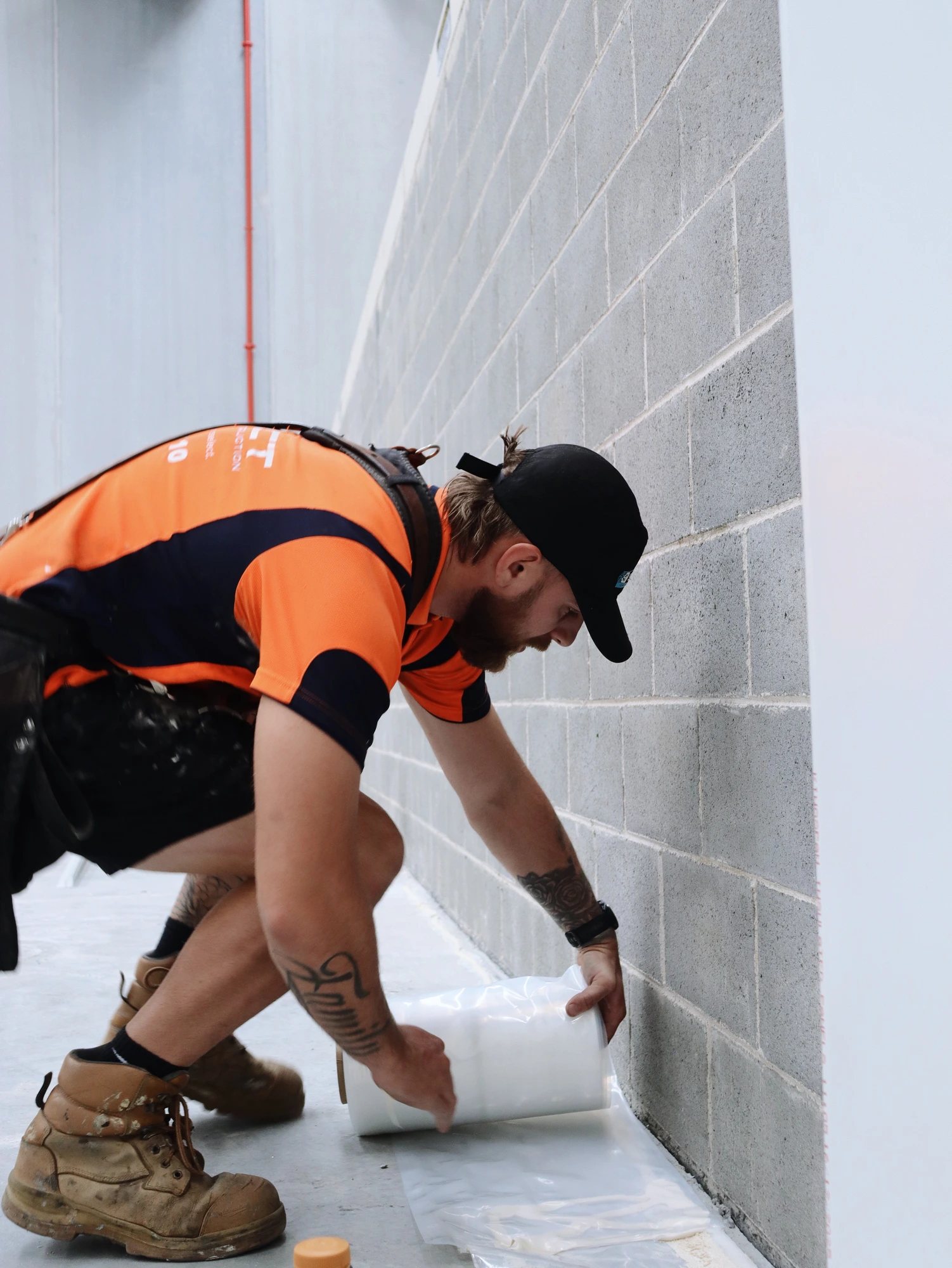 Installer rolling out the vapour seal along the base of the wall at Chullora, before the floor angle goes down